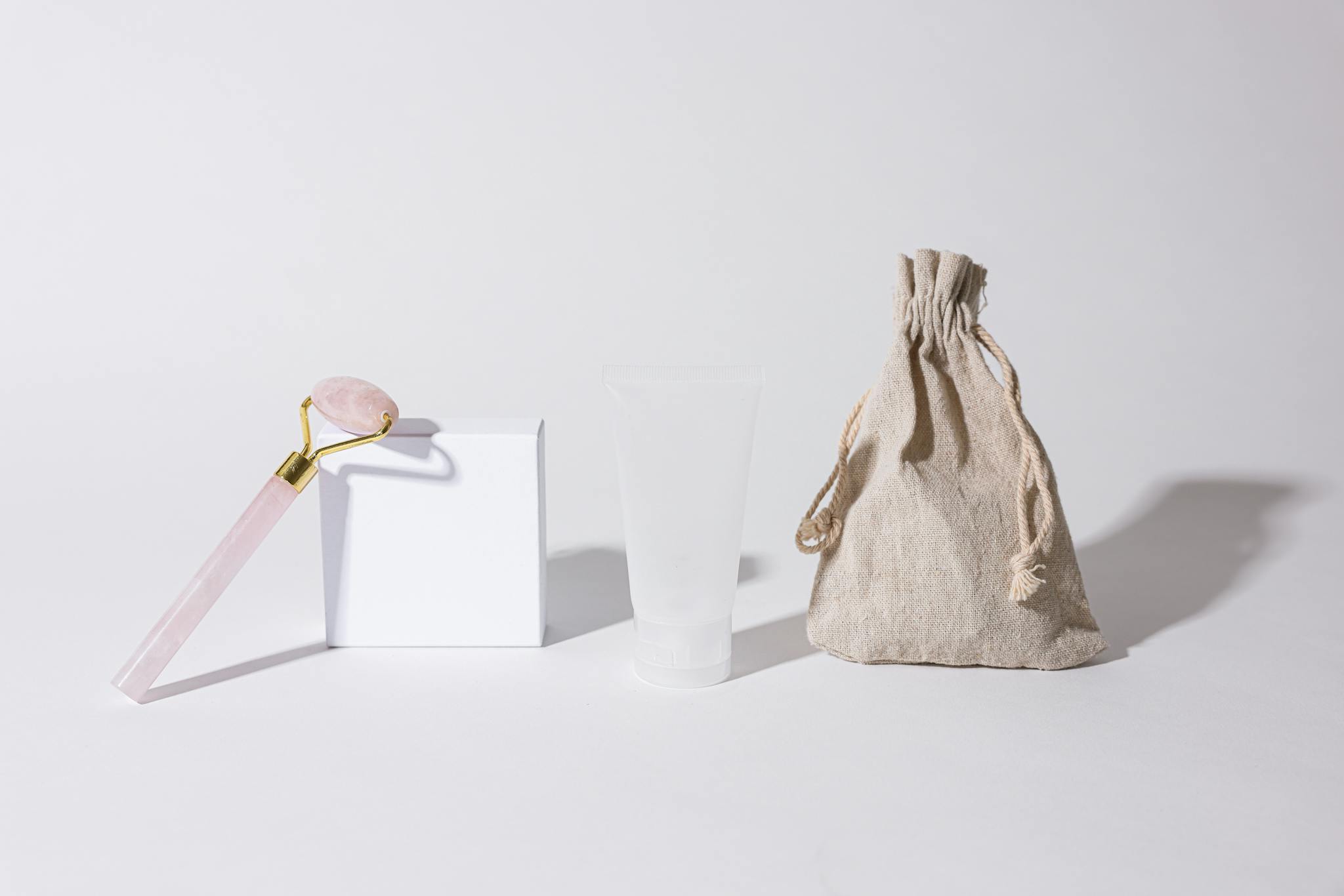 Cosmetic set with rose quartz roller and neutral packaging on white background.