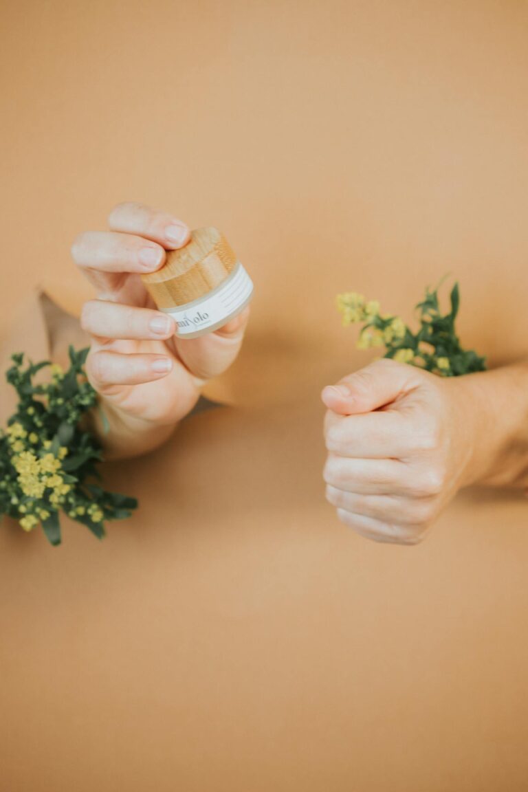 Eco-friendly skincare product held by hands through a brown backdrop with leaves.