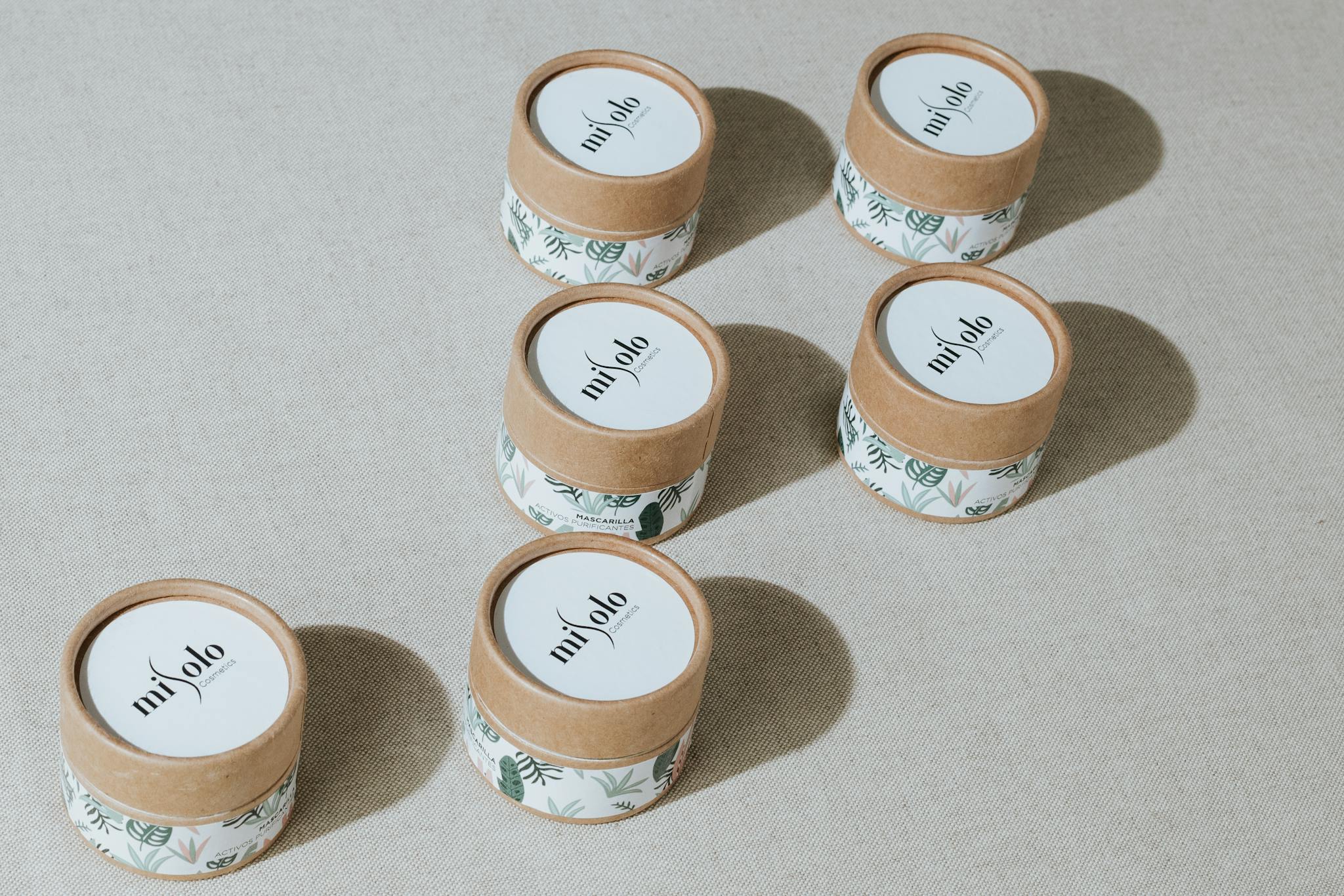 Minimalist display of six natural skincare product jars on a neutral background.